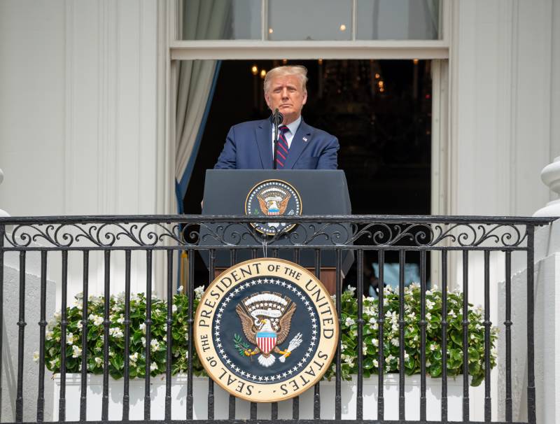 Donald Trump standing at a podium in front of the White House
